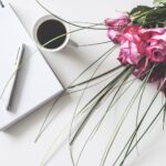 red rose flowers bouquet on white surface beside spring book with click pen and cup of cofffee